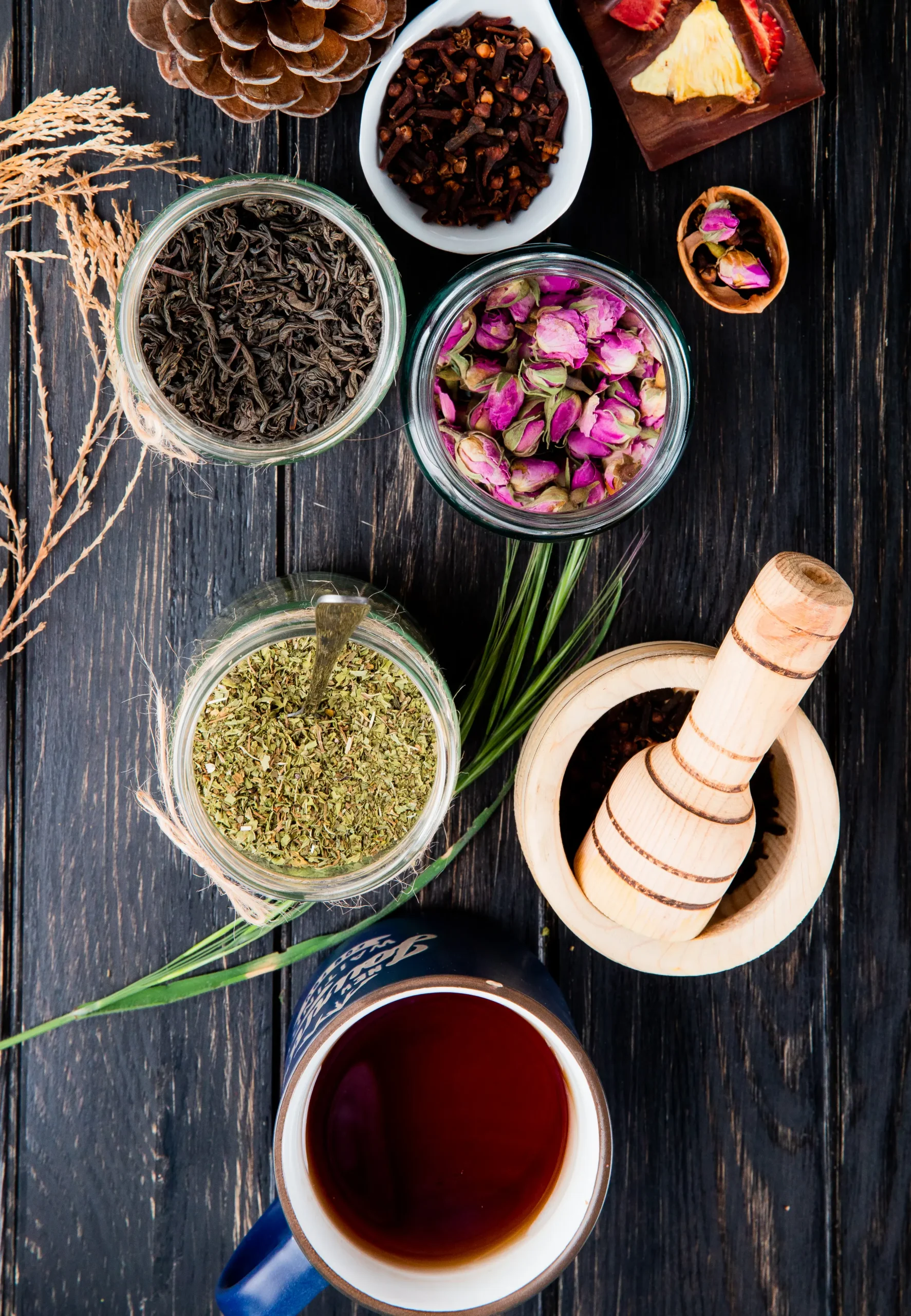 Top view various spices herbs dry black tea leaves peppermint rose buds clove spice black peppercorns glass jars black wood scaled